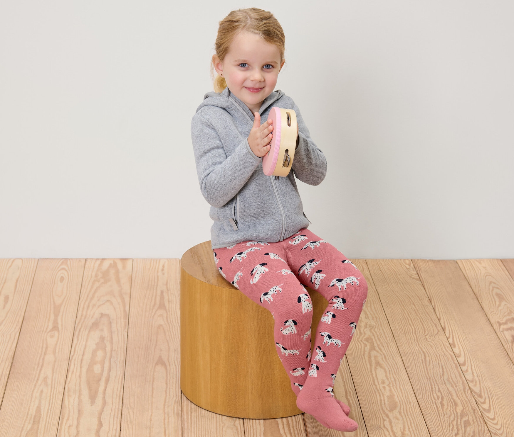 Egy lány ül és tamburázik, rózsaszín és szürke gyerek termo harisnyanadrágot visel.