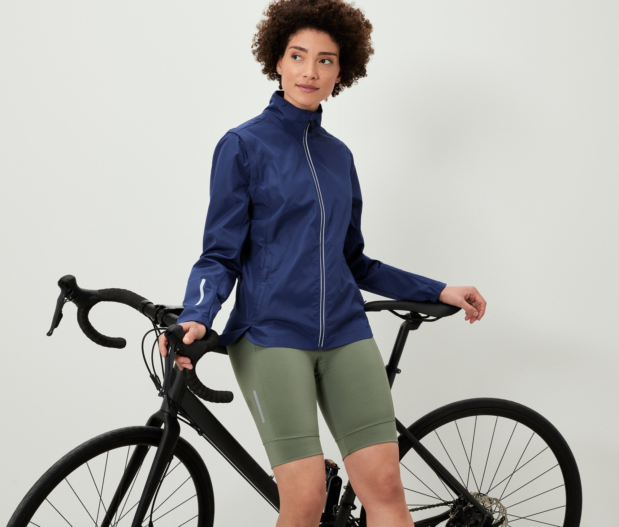 Egy nő a kerékpárjára támaszkodva egy 2 az 1-ben kerékpáros kabátot visel.