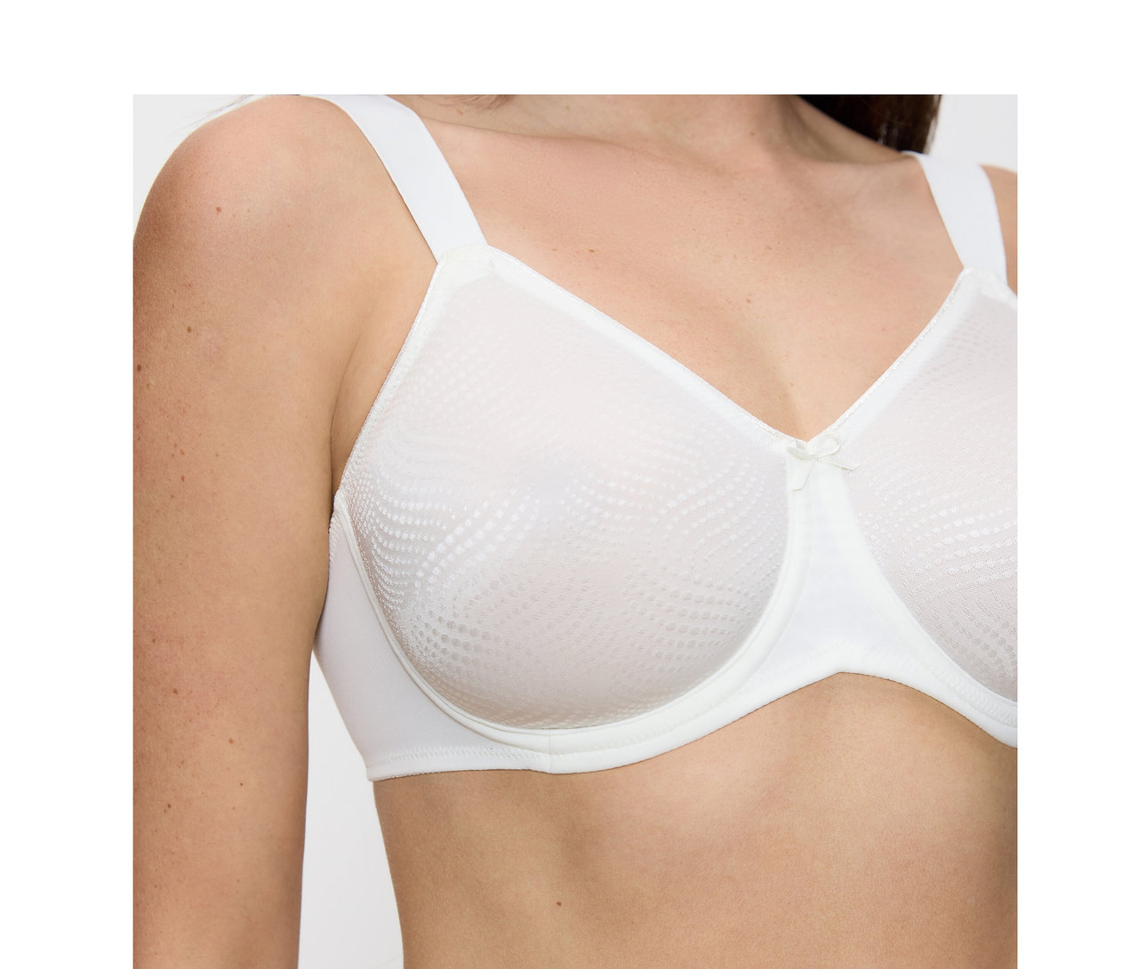 Nő visel egy vanília színű Triumph Essential »Minimizer W X« melltartót mintás kosarakkal és kis masnival.