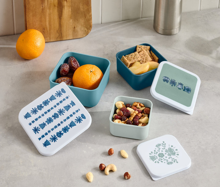 A pulton egy termosz és egy fa vágódeszka áll négy kis, nyitott, gyümölcsöt, kekszet és diót tartalmazó doboz, valamint négy különböző mintázatú fedő mellett.