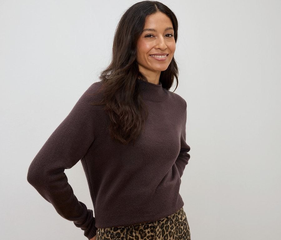 Sötét, hullámos hajú nő mosolyog, barna pulóvert és leopárdmintás szoknyát visel.