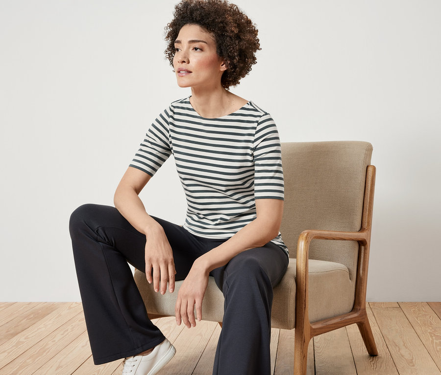 Nő ül egy széken, és zöld csíkos, félhosszú ujjú felsőt visel.