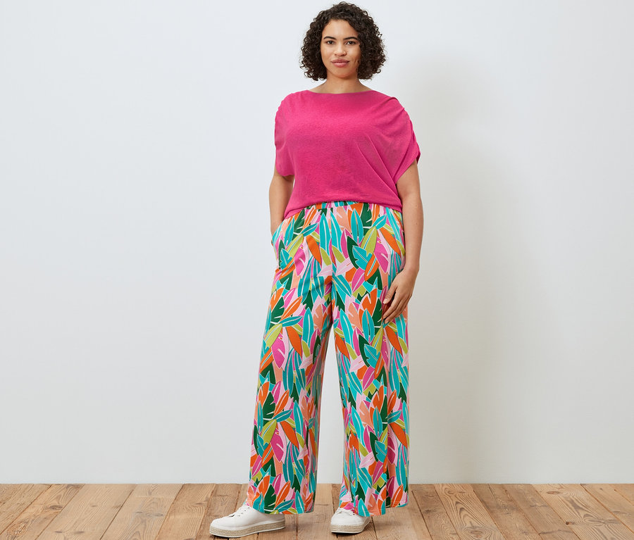 Nő pózol lentartalmú kevert anyagból készült pólóban és nyomott mintás, színes palazzo nadrágban.