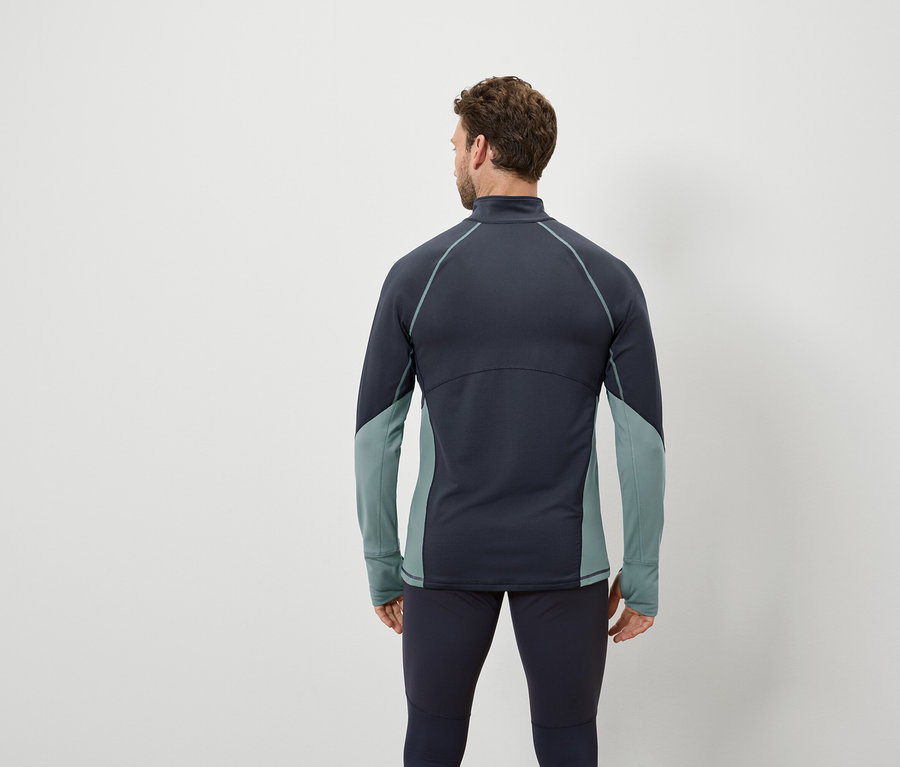 Hátulról látható férfi sötétkék hosszú ujjú felsőt és sötétkék leggingset visel, kékeszöld betétekkel.