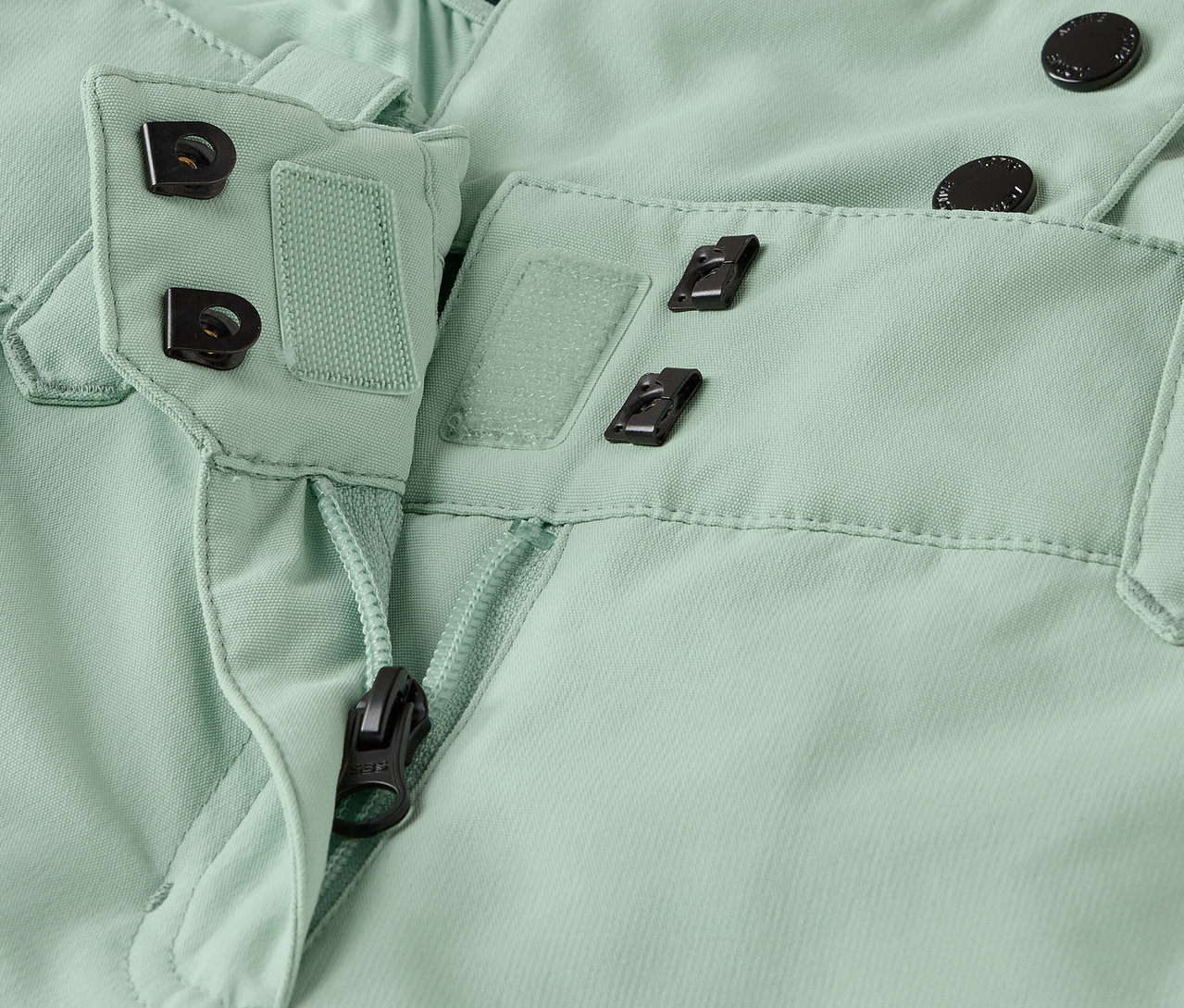 Világoszöld nadrág részlete cipzárral és gombos záródással.