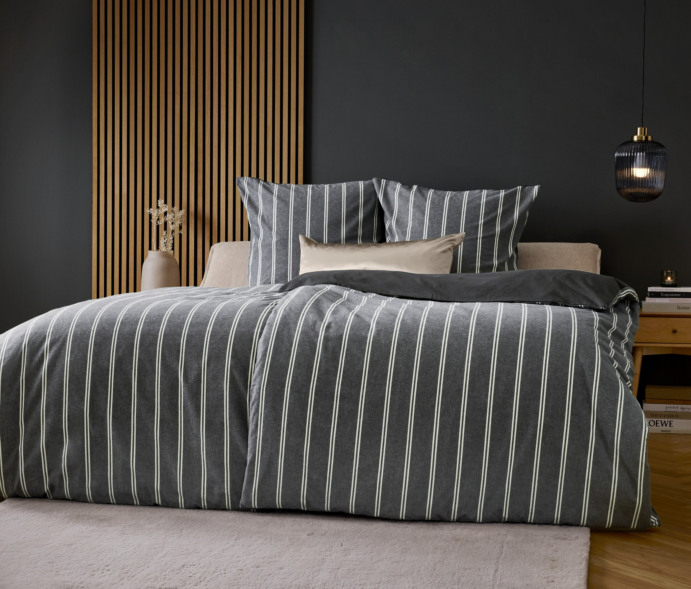 Egy ágy szürke-fehér csíkos ágyneművel, szürke fal előtt.