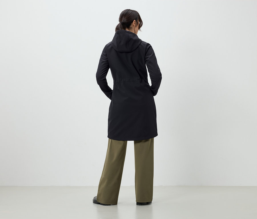 A kamerának háttal álló nő fekete kabátot és zöld nadrágot visel.