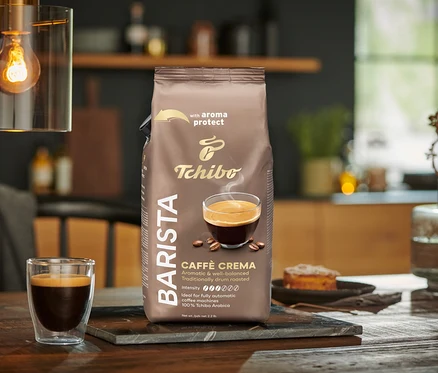 Egy csomag BARISTA Caffè Crema - 1x1 kg szemes kávé egy asztalon áll egy pohár kávé mellett.