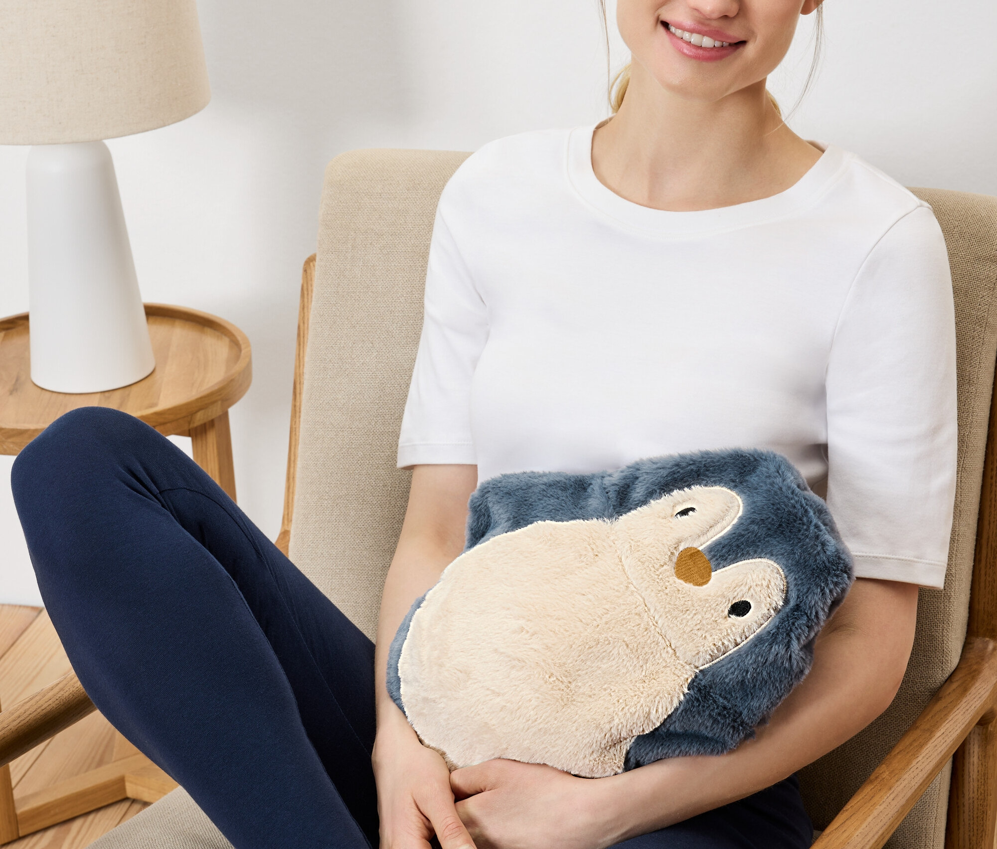 Egy nő ül egy székben, és egy plüss pingvin melegítőpárnát tart.