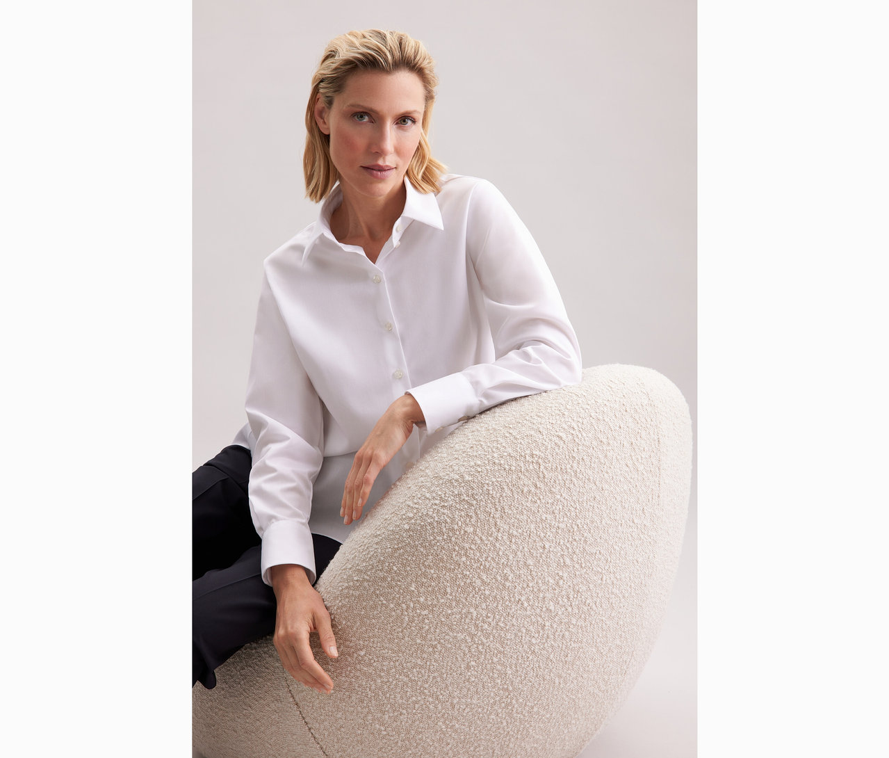 Nő ül egy széken és fehér Seidensticker túlméretes hosszú ingblúzt visel.