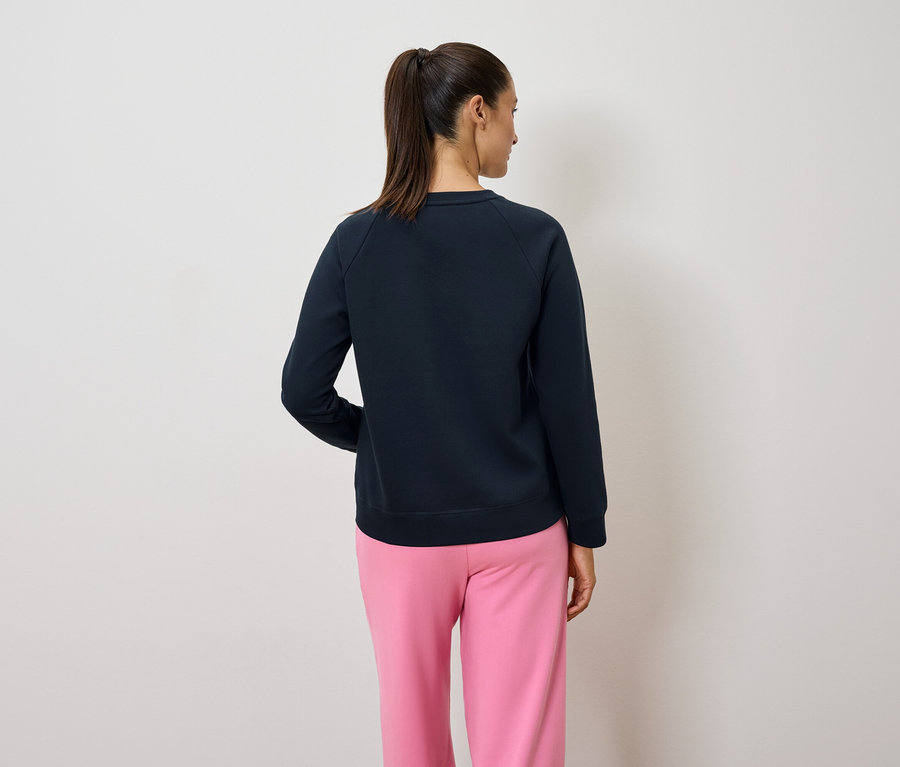 Hátulról látható egy lófarokos nő sötétkék pulóverben és rózsaszín nadrágban.