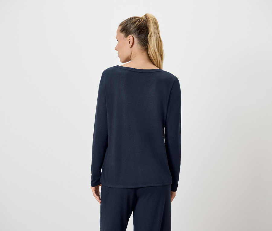 Hátulról látható egy szőke hajú, copfba kötött nő. Sötétkék, hosszú ujjú felsőt és nadrágot visel.