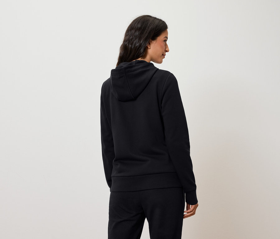 Egy hátulról látható nő fekete kapucnis pulóvert és fekete nadrágot visel.