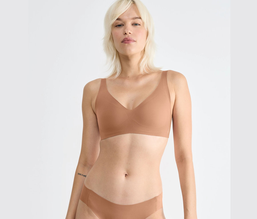 Szőke nő visel egy barna sloggi ZERO Feel 2.0 puha melltartót.