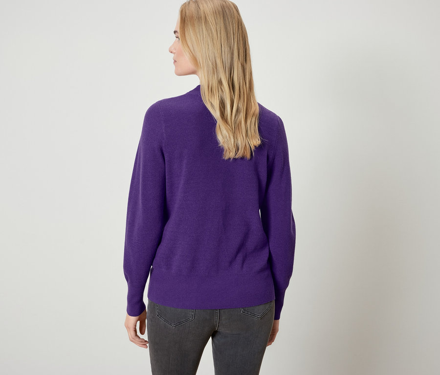 Hátulról látható egy szőke hajú nő lila pulóverben és szürke farmerben.