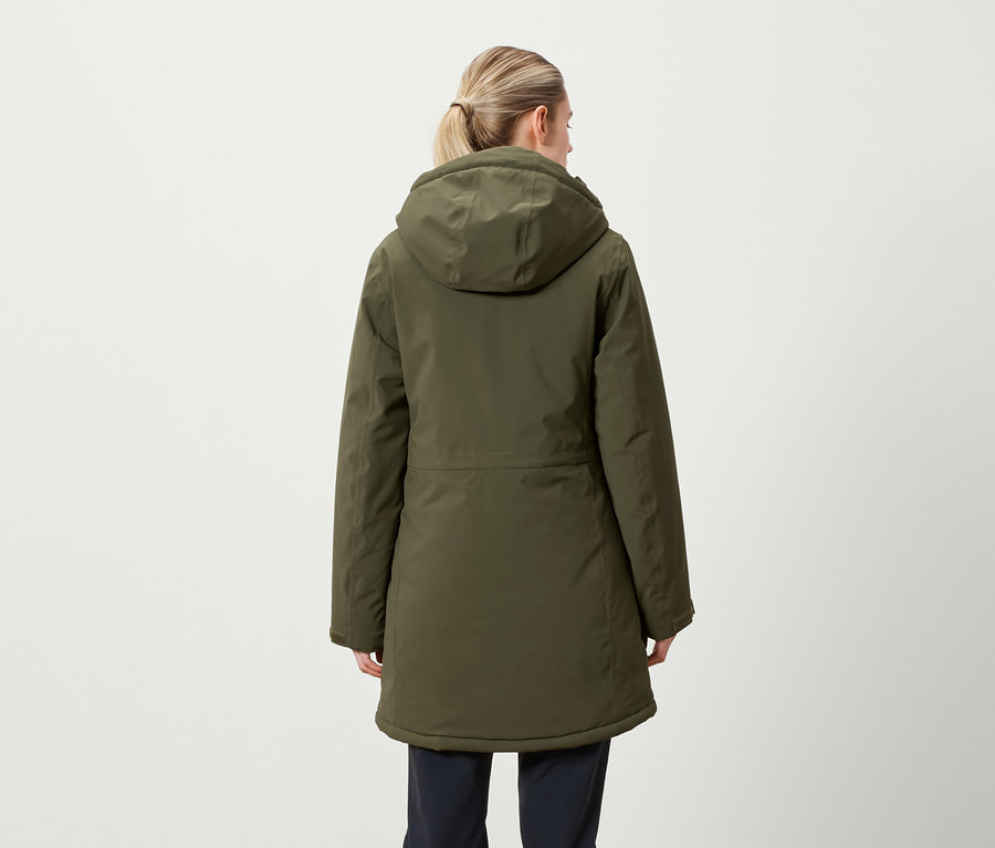 Hátulról látható egy szőke hajú, copfba fogott nő, aki olívazöld, kapucnis télikabátot visel.