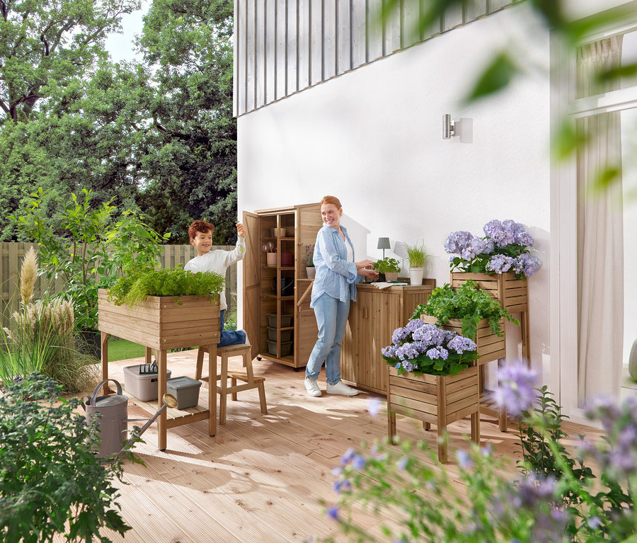 Egy fiú és egy nő kerti bútorokkal és növényekkel foglalatoskodik egy fa teraszon.