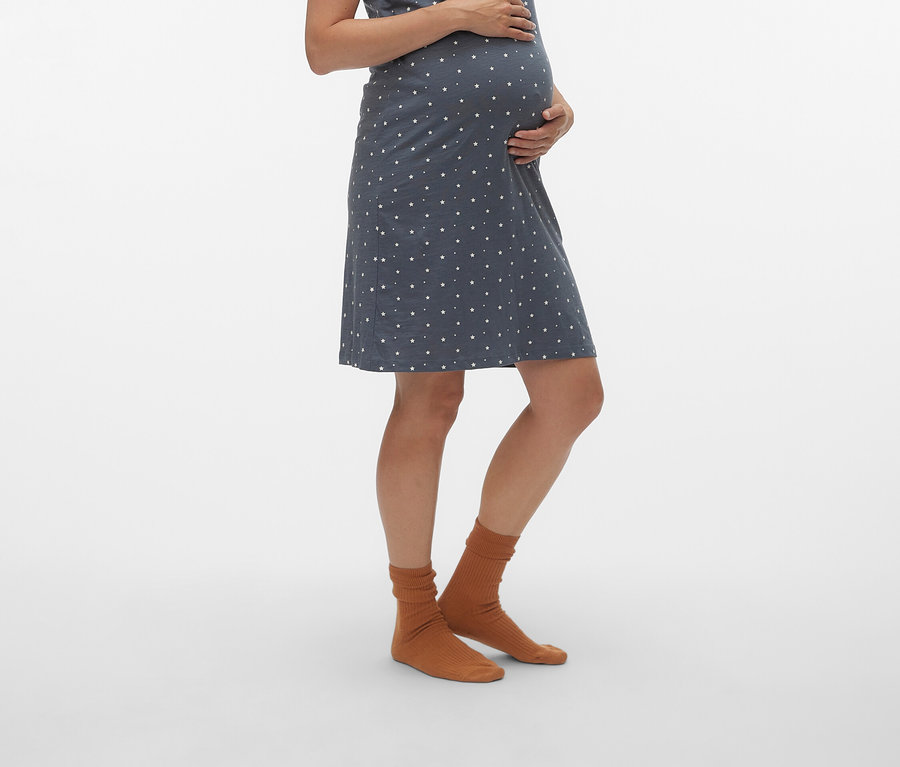 Terhes nő visel kék, fehér pöttyös kismama ruhát és barna zoknit.