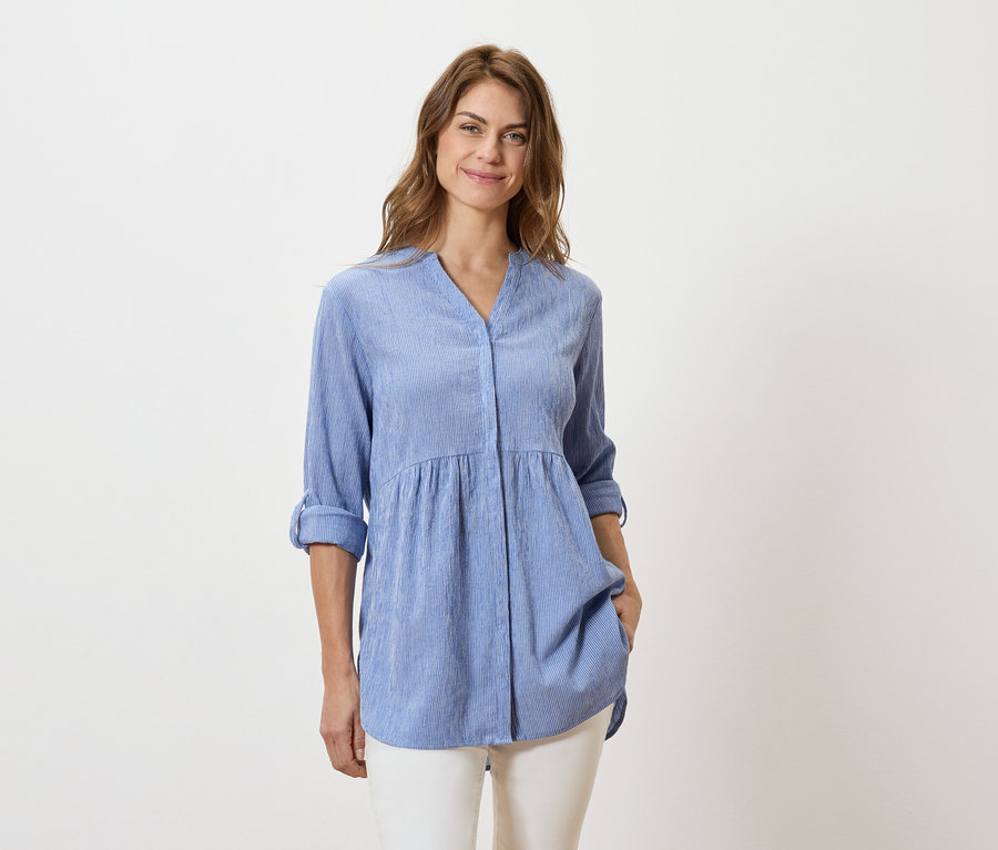 Nő világoskék, hosszú ujjú blúzt és fehér nadrágot visel.