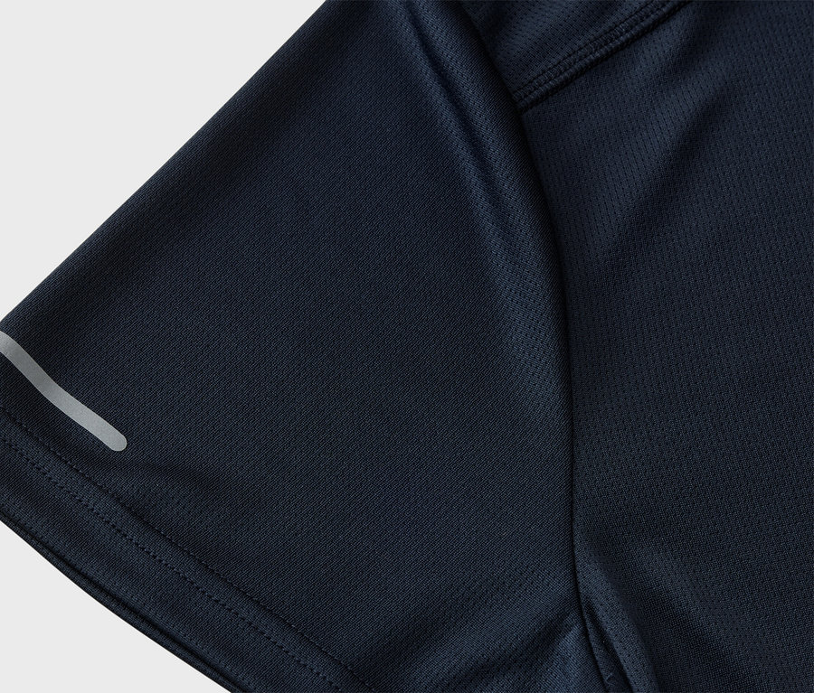 Egy sötétkék, hálós szerkezetű sportpóló közeli képe, melynek ujján fényvisszaverő csík található.