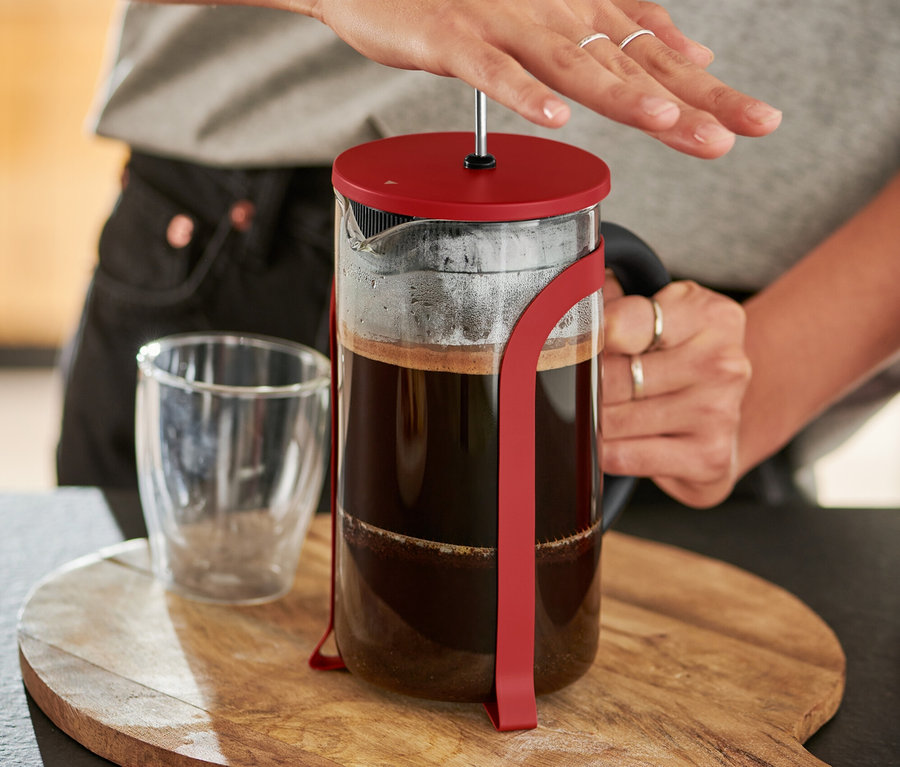 Nő nyomja a piros, 800 ml-es, 6 csészés dugattyús kávéfőzőt egy fa deszkán.