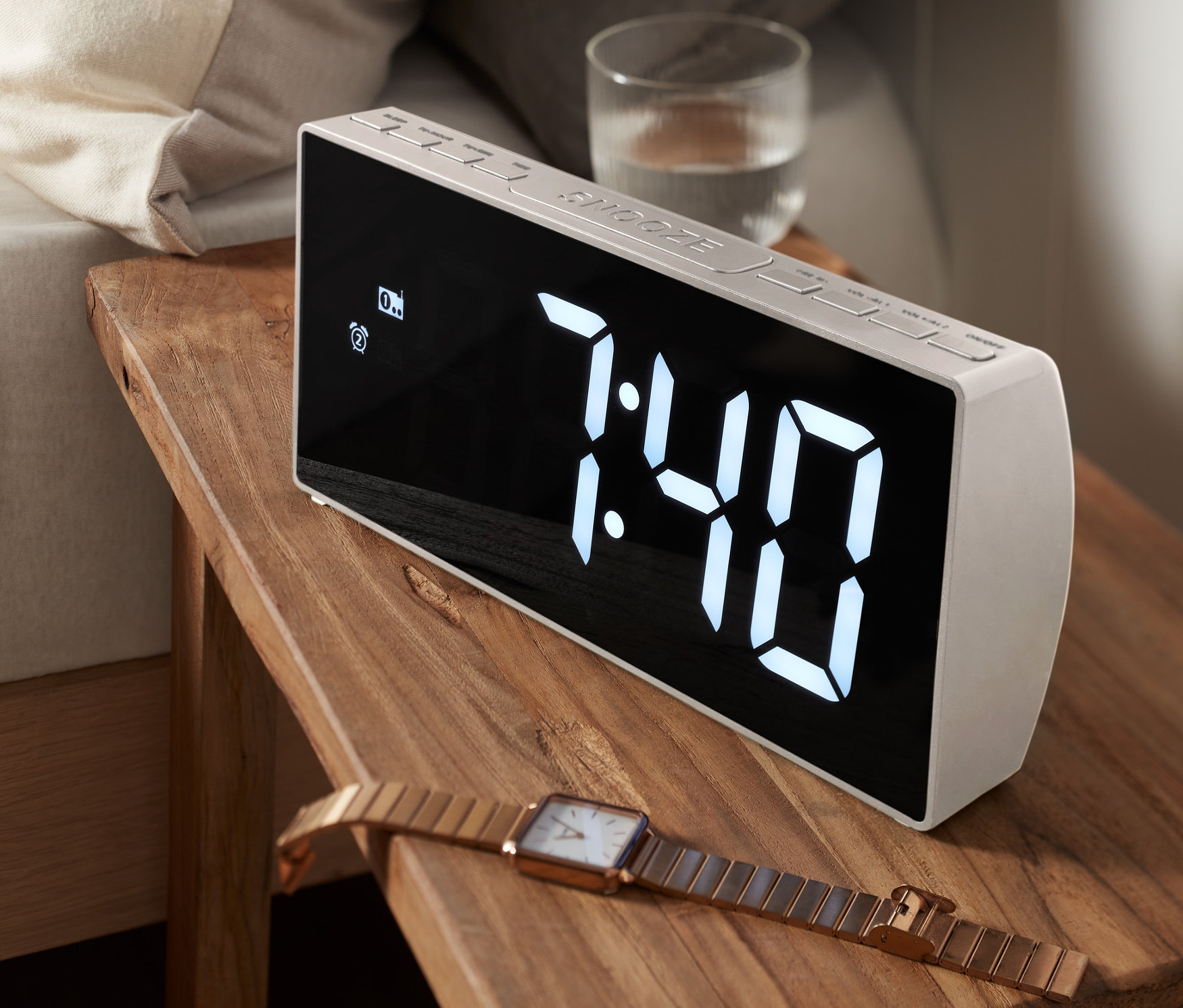 Egy XXL rádiós ébresztőóra áll egy fa éjjeliszekrényen egy ágy mellett. A kijelzőn 7:40-es idő látható.