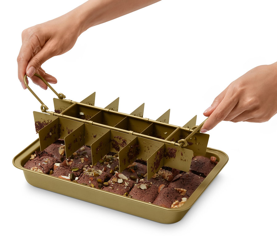 Egy személy egy brownie sütőformát tart egy tepszi fölé, amiben felszeletelt brownie-k vannak.