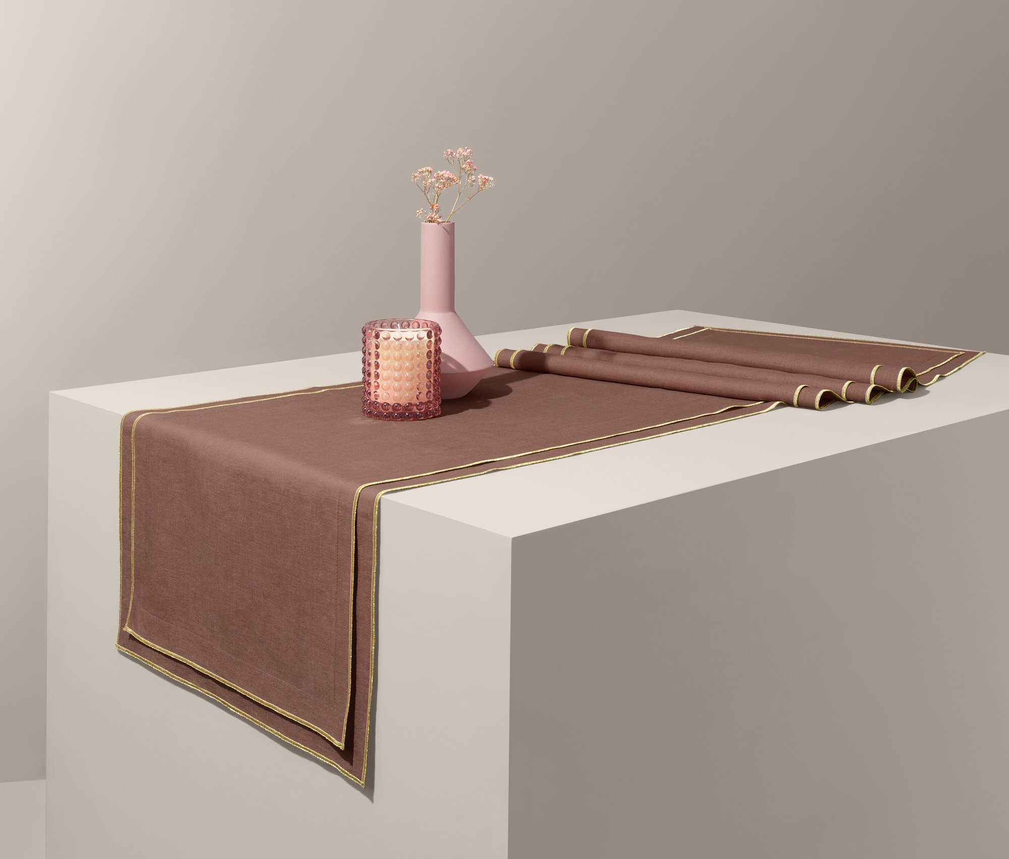 Asztali futó, váza virágokkal és gyertya egy fehér talapzaton.