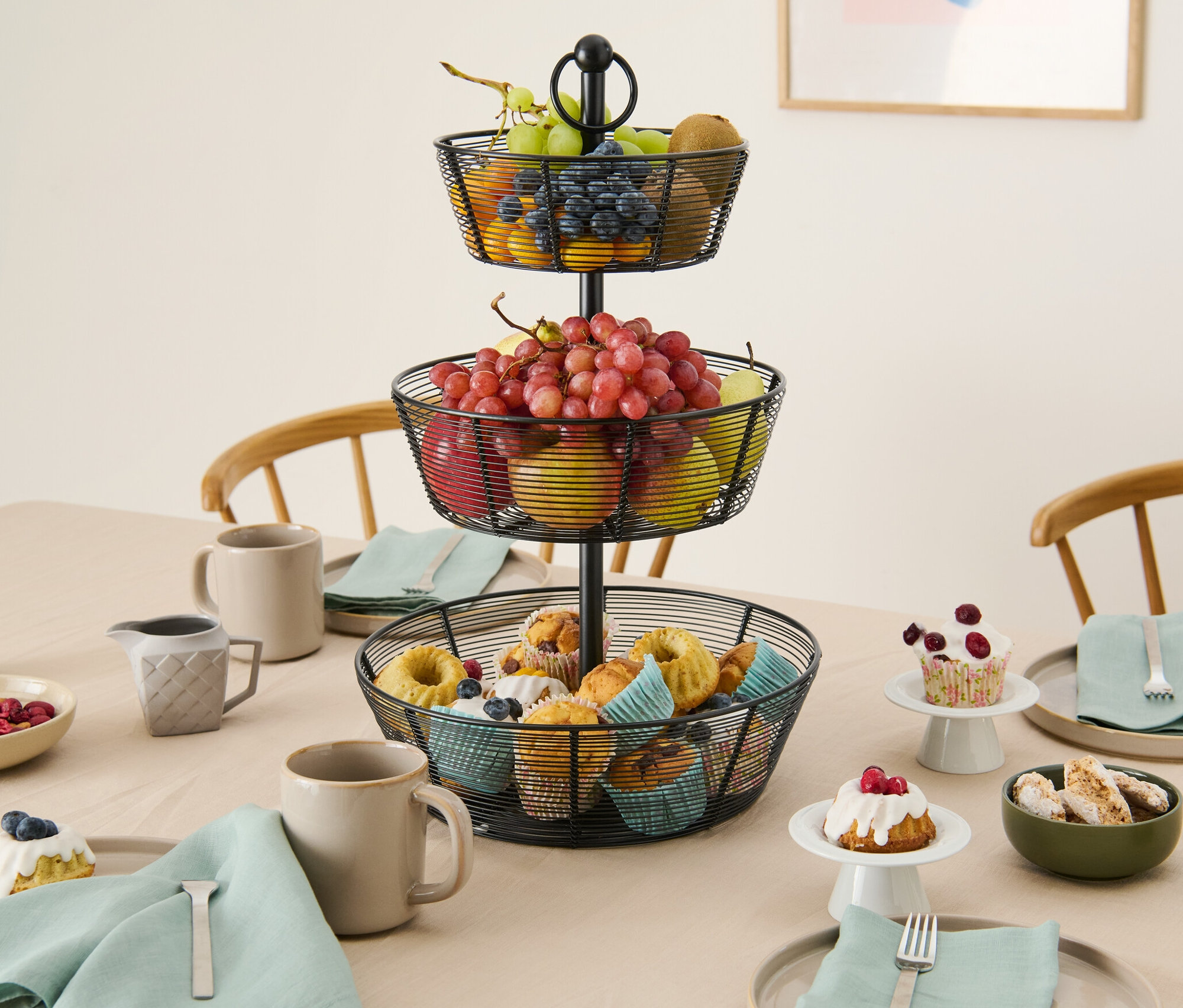 Egy háromszintes, gyümölcsökkel és muffinokkal teli emeletes kínáló áll az asztalon.