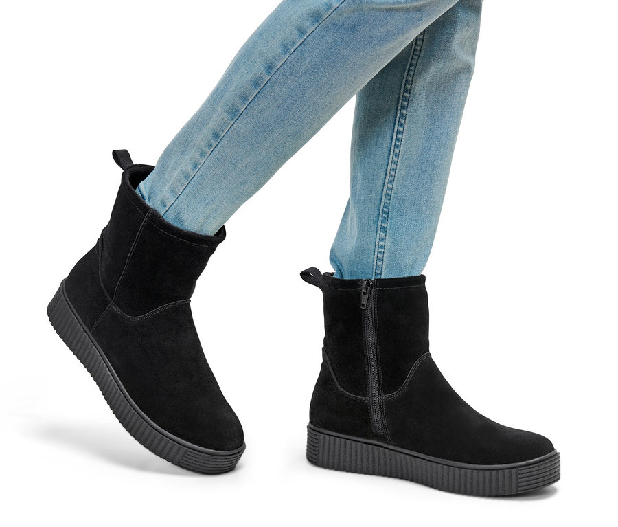 Farmerben és fekete női velúrbőr csizmában lévő lábak.