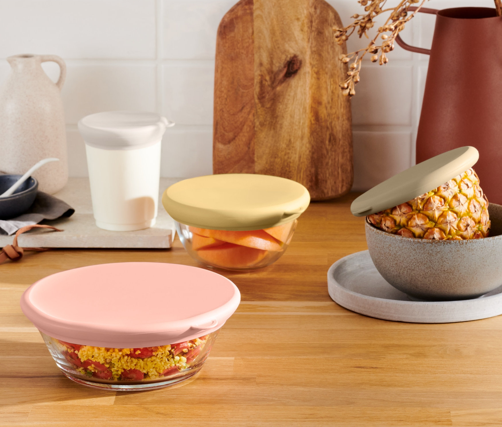 Üveg tálak színes 4 szilikon frissentartó fedél szettben egy fa asztallapon.