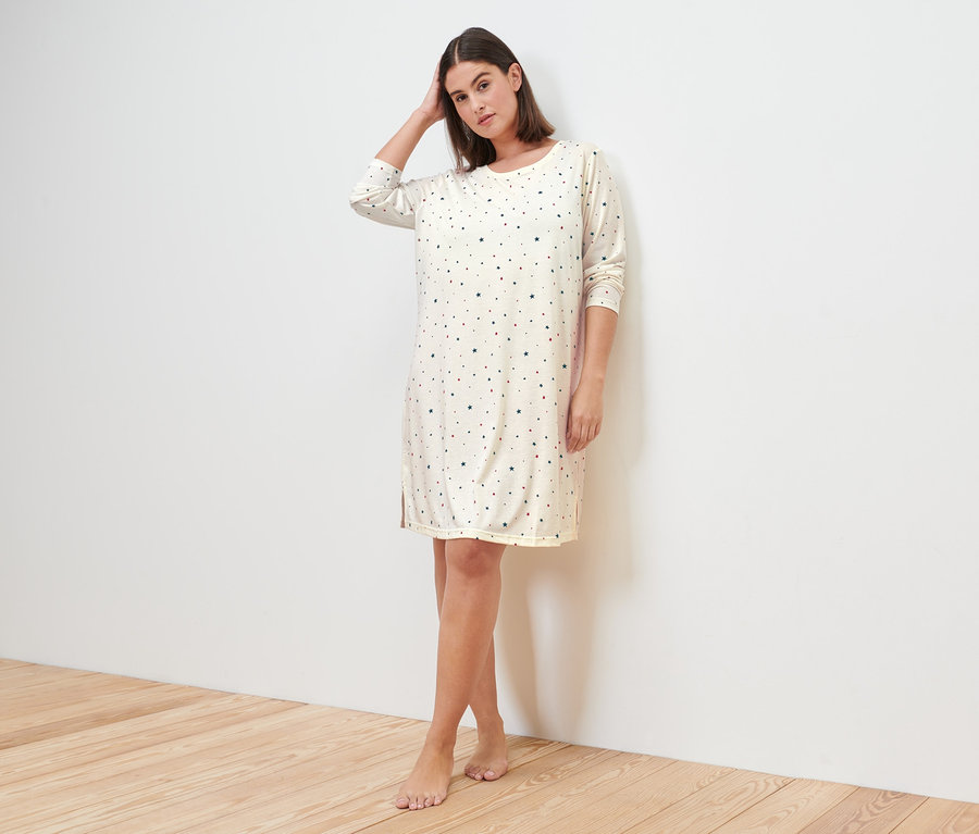 Nő pózol egy krémszínű hálóingben.