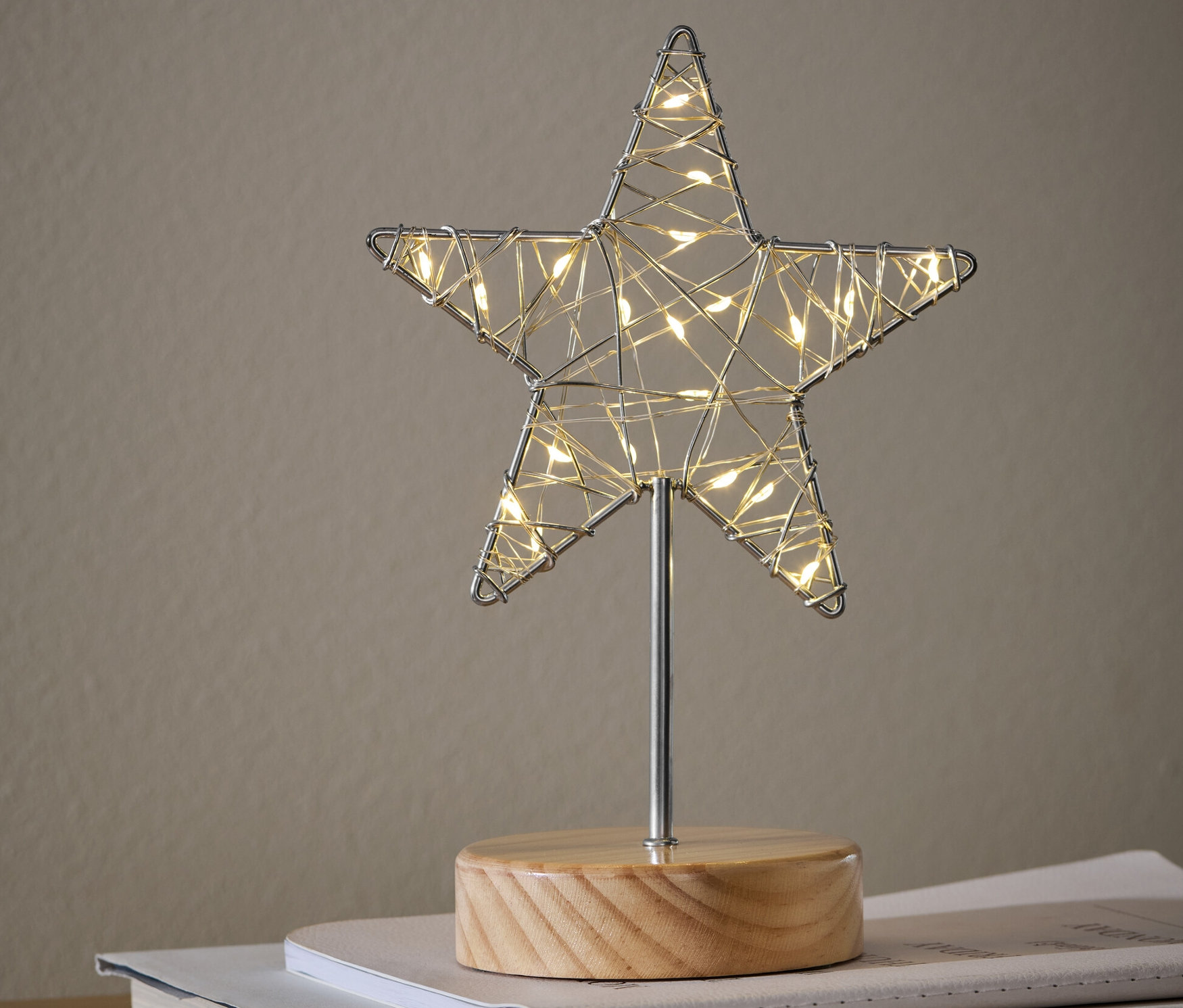 Egy LED-es csillag dísz áll könyveken egy szekrényen.