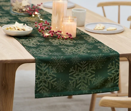 Az asztalon egy zöld jacquard asztali futó karácsonyi díszekkel.