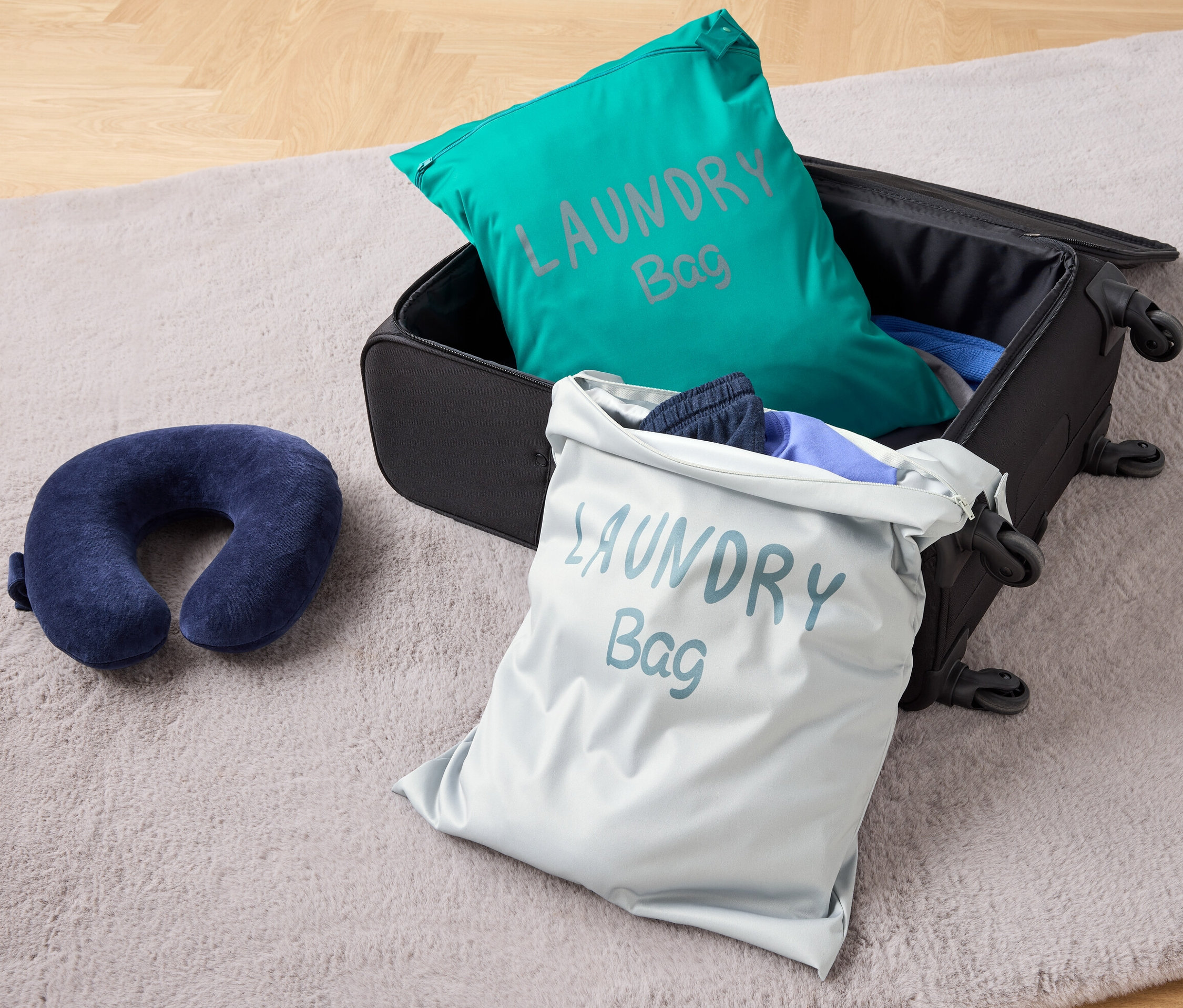 A padlón egy nyitott bőrönd található, benne két szennyestartó zsák utazáshoz és egy utazópárna.