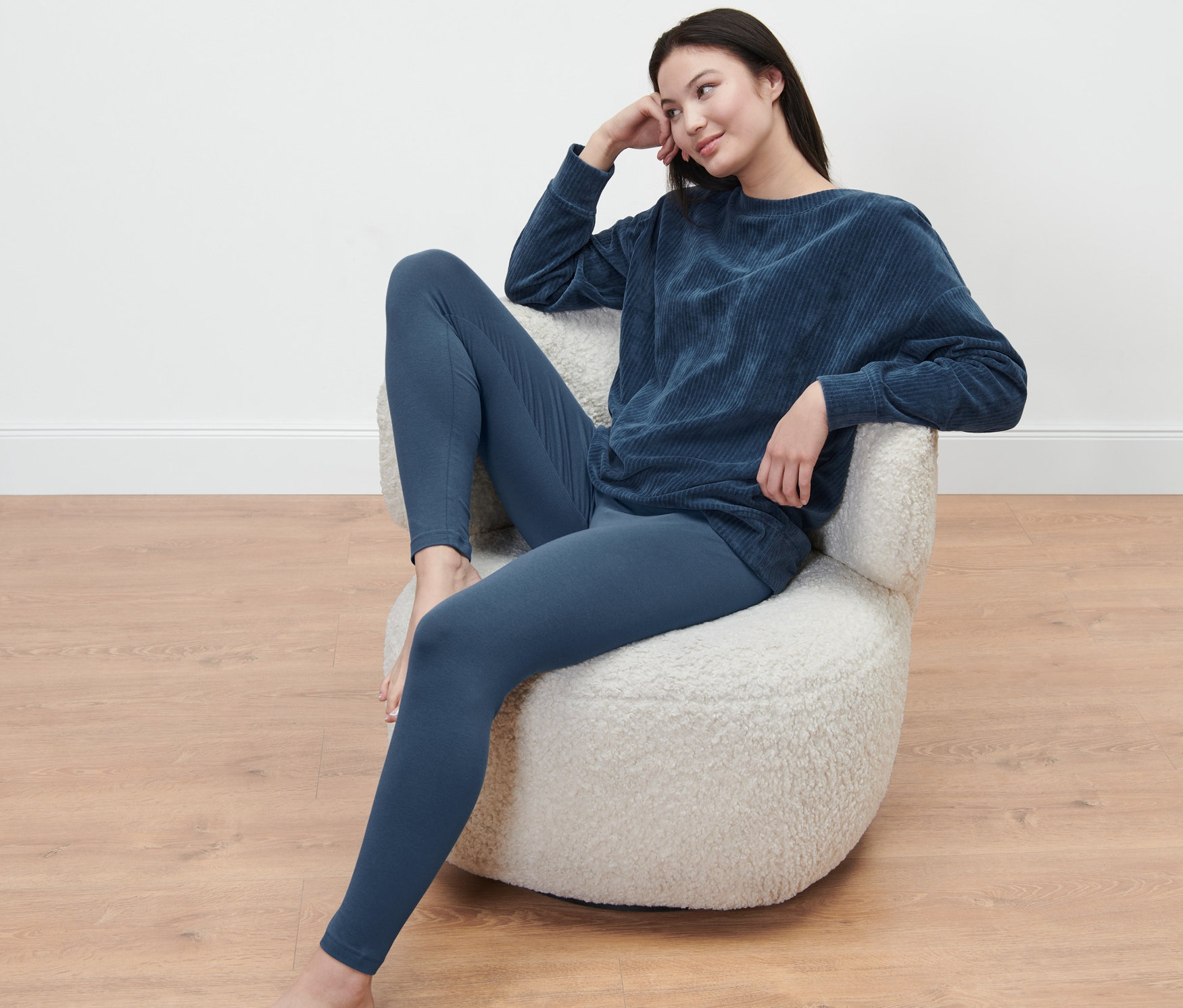 Nő ül egy székben, sötétkék plüss pizsamát és leggingset visel.
