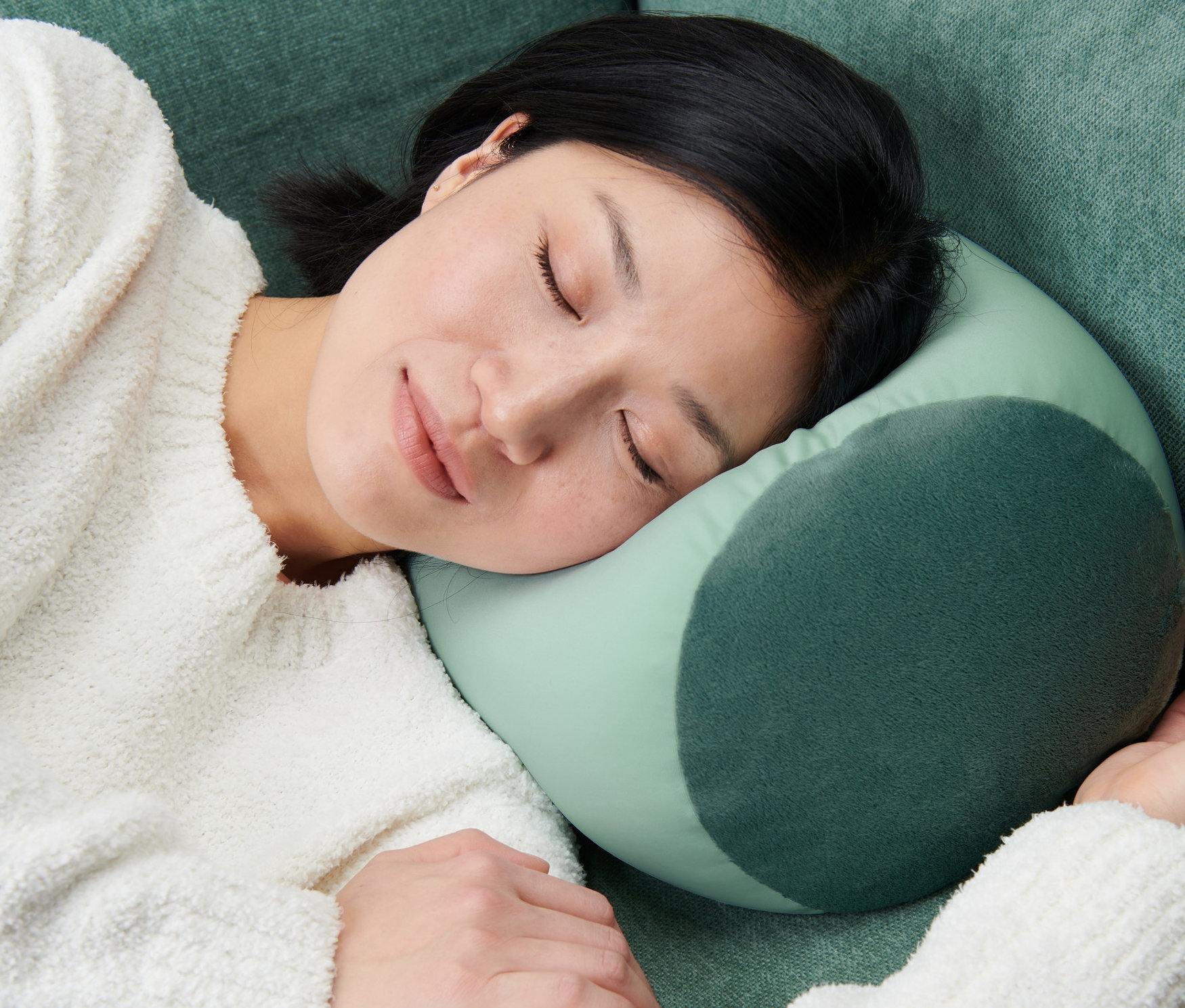 Nő alszik egy zöld kanapén egy relaxációs párnán.