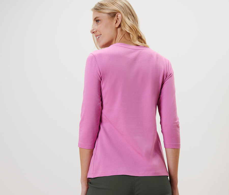 Egy nő a válla fölött hátra néz, rózsaszín, 3/4-es ujjú felsőt visel.