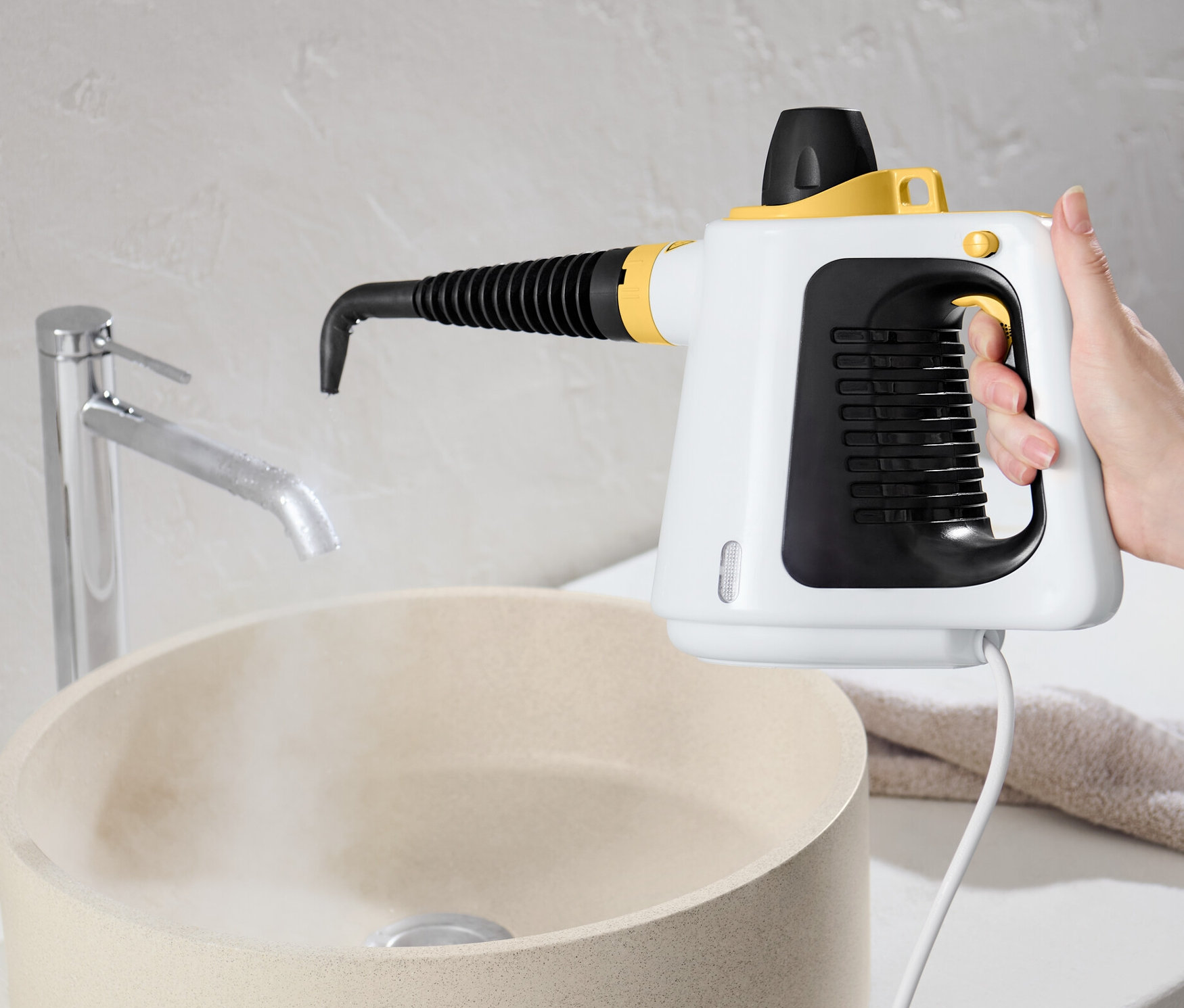 Egy kéz gőztisztítót tart a mosdókagyló fölé.