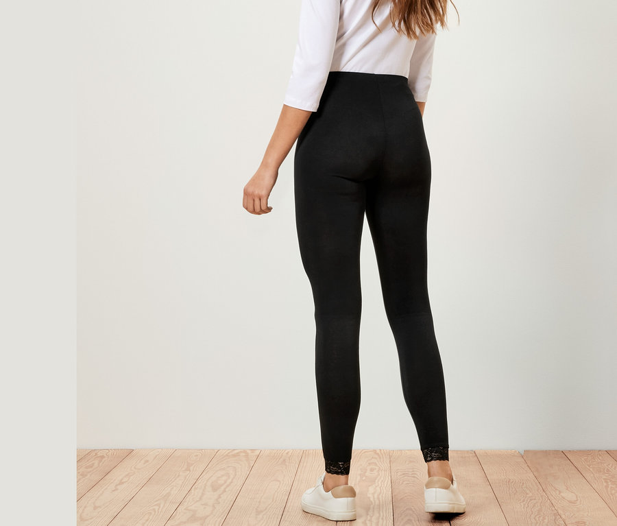 Hátulról látható nő fekete, csipkeszegélyes leggingset, fehér felsőt és fehér tornacipőt visel.