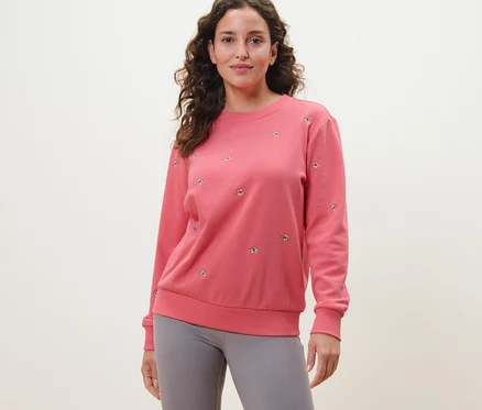 Nő visel rózsaszín, hímzett szabadidőfelsőt és szürke leggingset.