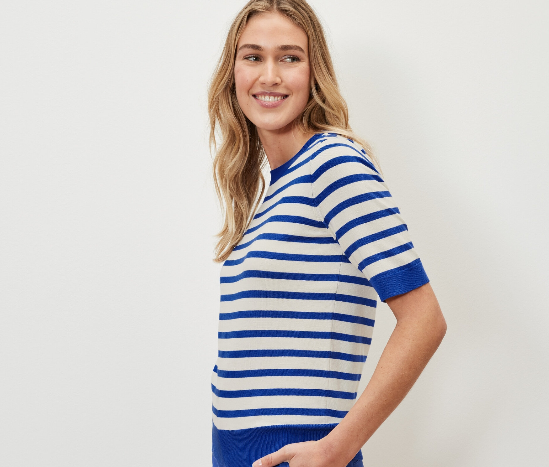 Nő visel egy csíkos, vékony kötött pulóvert és kék nadrágot.