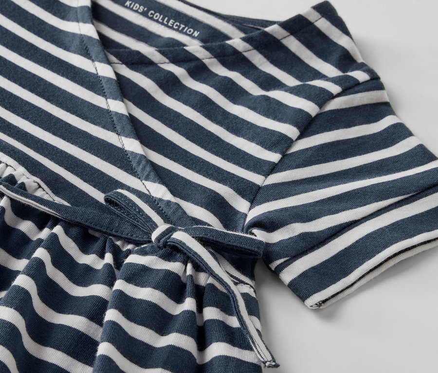 Közeli kép egy kék-fehér csíkos, derékkötős gyerek jersey ruháról.