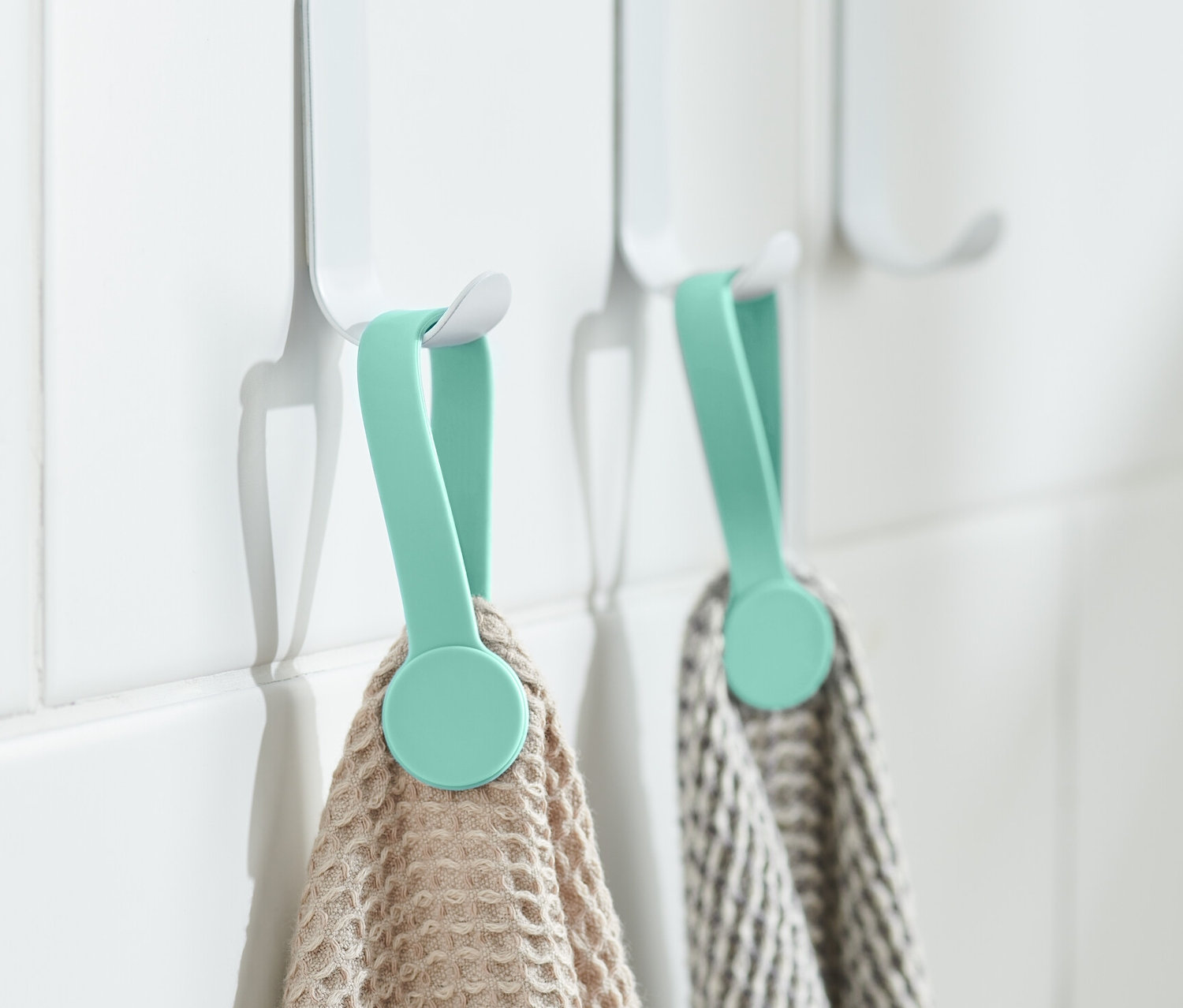 Két mágneses csipesz tart törölközőket fehér akasztókon a falon.