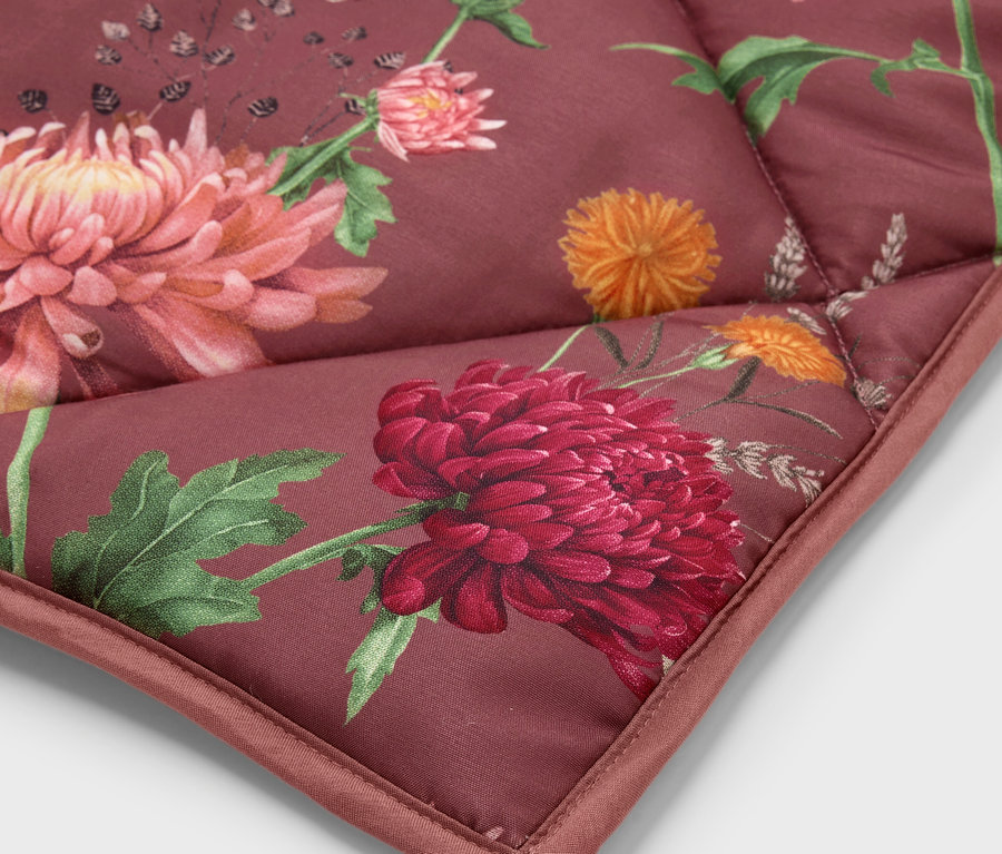 Egy piros, narancssárga és zöld színű virágmintás, steppelt takaró sarkának közeli felvétele.