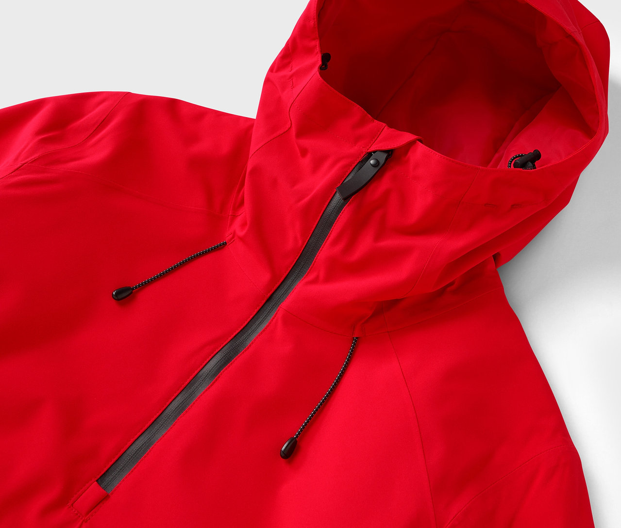 Egy piros, kapucnis kabát részlete fekete cipzárral.