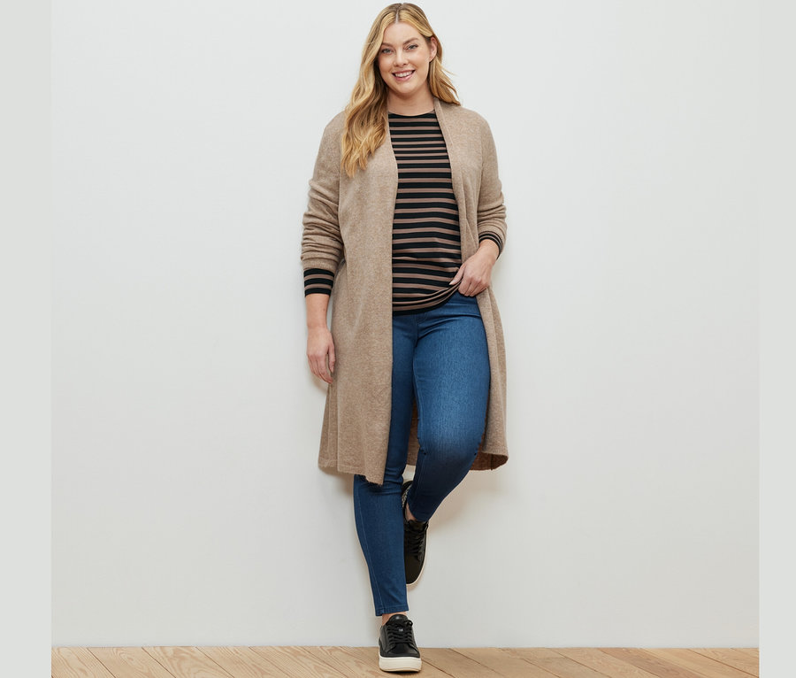 Nő pózol jeggingsben, egy fekete-barna csíkos hosszú ujjú felsőben és egy nyitott, hosszú kardigánban.