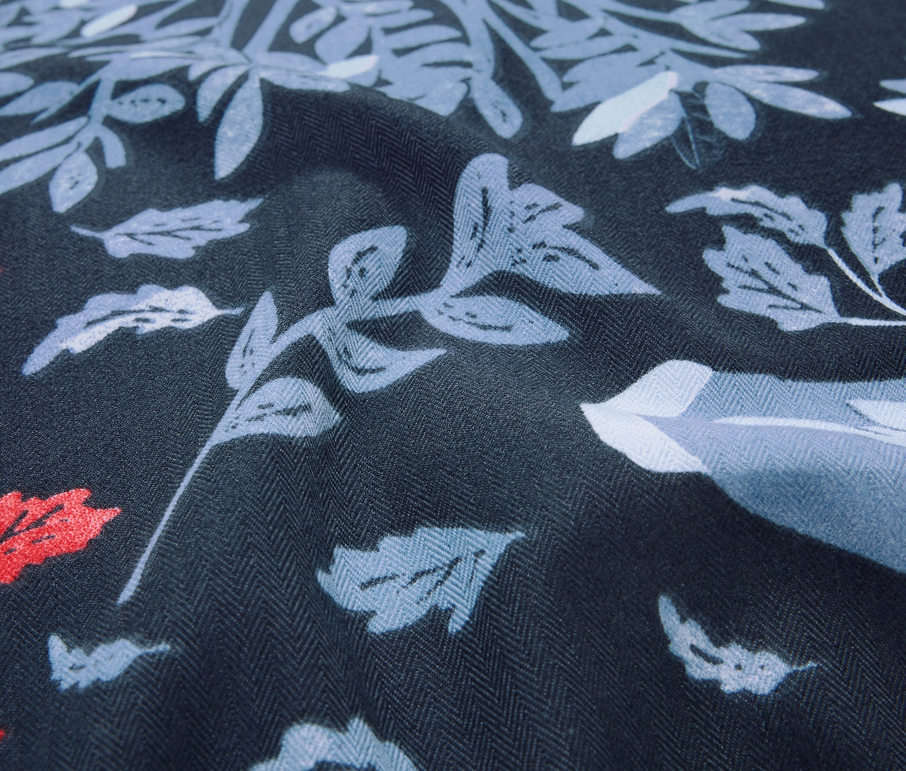 Közeli felvétel egy sötétkék szövetről, kék és piros árnyalatú levél- és virágmintával.
