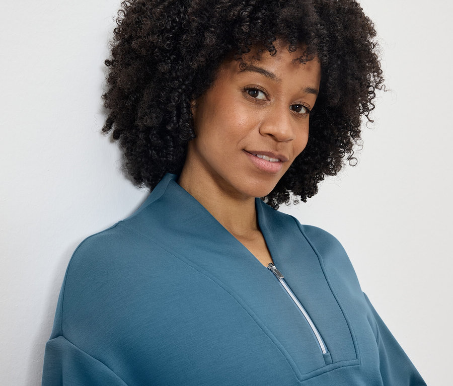 Portré egy mosolygó, afro frizurás nőről, kék-zöld cipzáros pulóverben.
