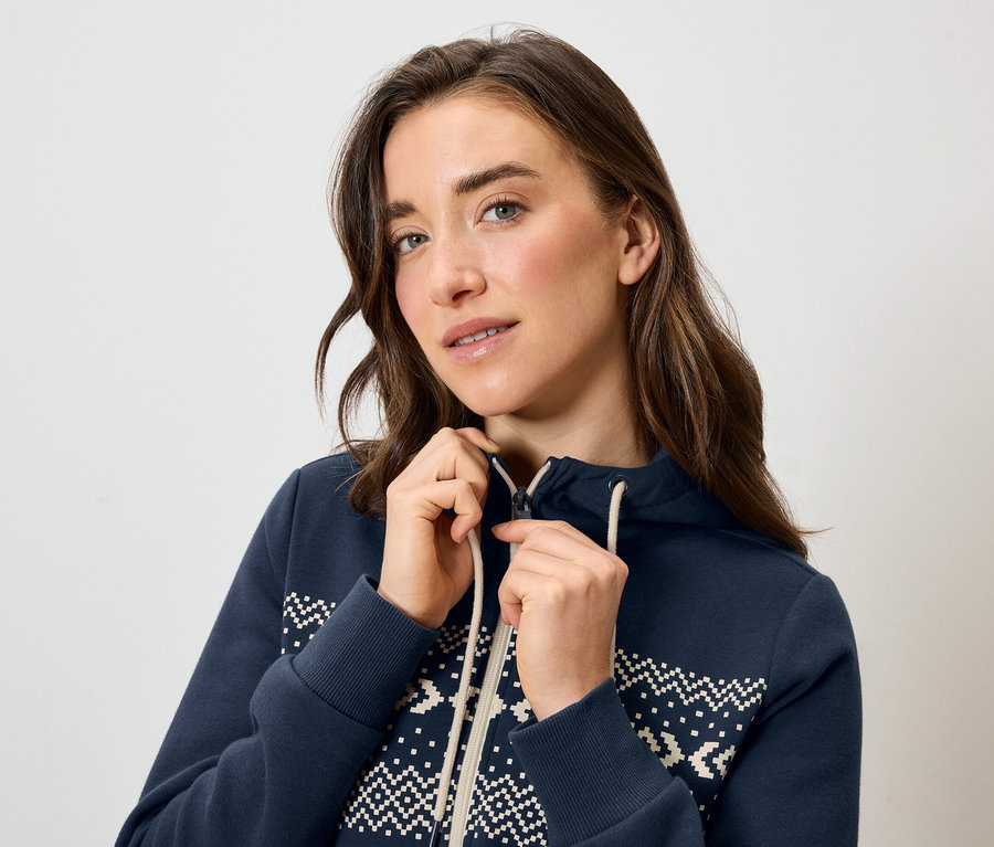 Egy nő kék, fehér mintás kapucnis pulóvert cipzároz.